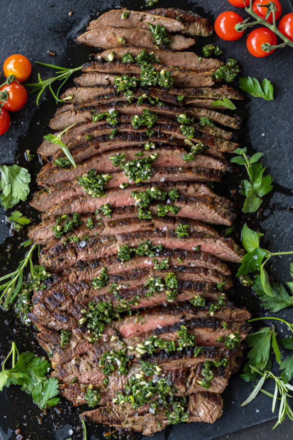 Chimichurri Steak sliced on a serving tray and herbs.