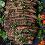 Chimichurri Steak sliced on a serving tray and herbs.