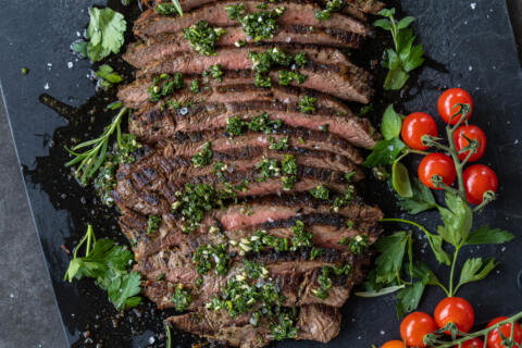 Chimichurri Steak sliced on a serving tray and herbs.