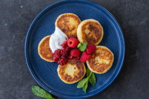 Syrniki plated with jam and sour cream.