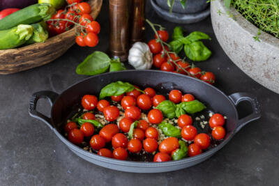 Cherry tomatoes, garlic, oil and basil in a pan.