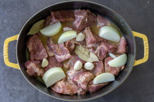 Seasoned pork, with juice and onion, garlic and bay leaves in a pot.