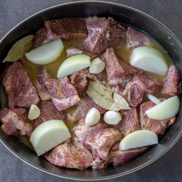Seasoned pork, with juice and onion, garlic and bay leaves in a pot.