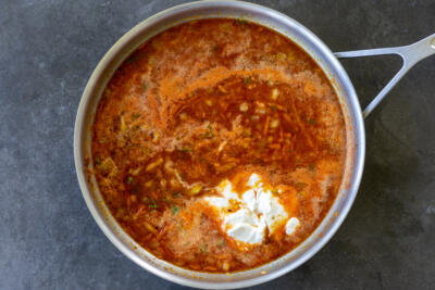 Sour cream added to tomato sauce in a pan.