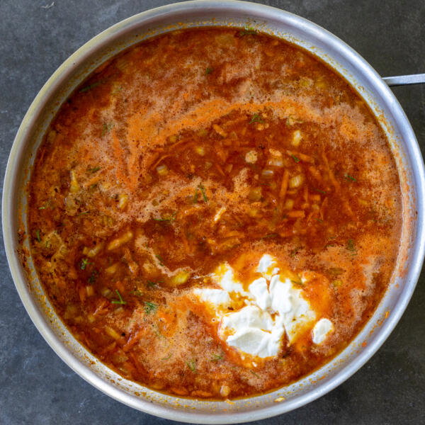 Sour cream added to tomato sauce in a pan.