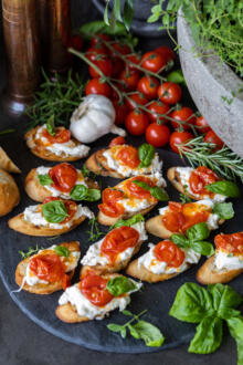 Burrata Crostini with Blistered Tomatoes on a tray and other ingredients from recipe around.