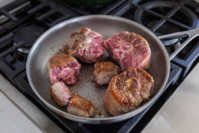 Oxtail getting browned in a pan.