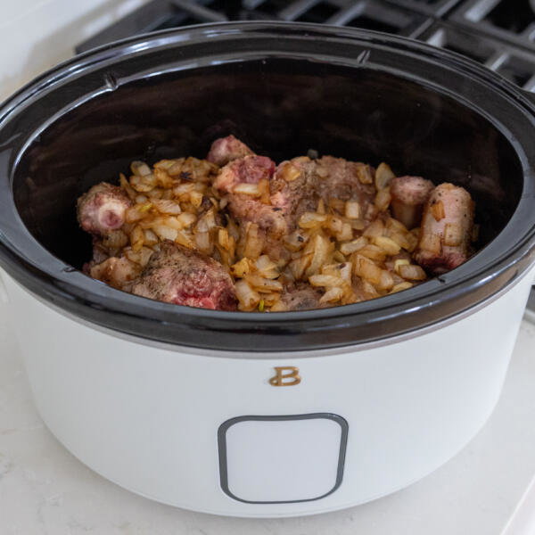 Oxtail and onion in a slow cooker with seasoning.