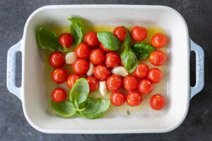 Tomatoes in a tray with garlic, oil and seasoning.