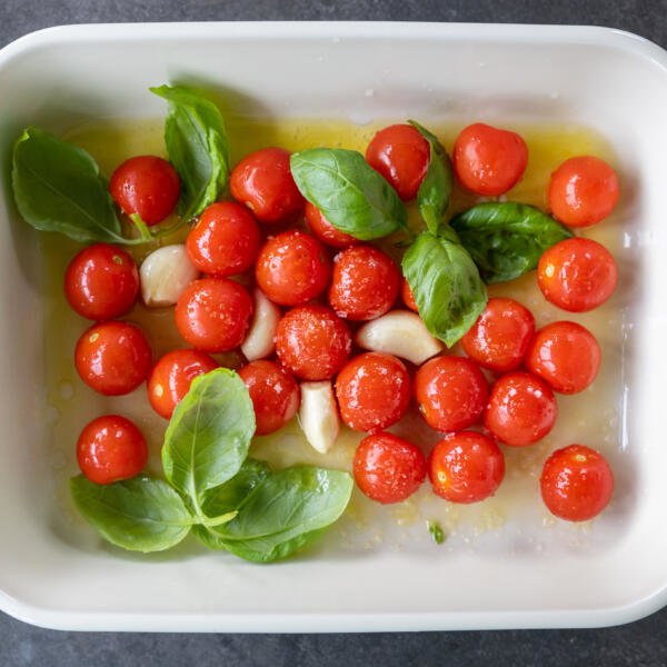 Tomatoes in a tray with garlic, oil and seasoning.