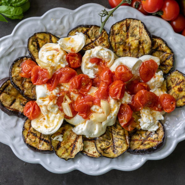 Eggplant, burrata and roasted tomatoes on a plate.