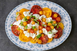 Tomatos, burrata and herbs on a plate.