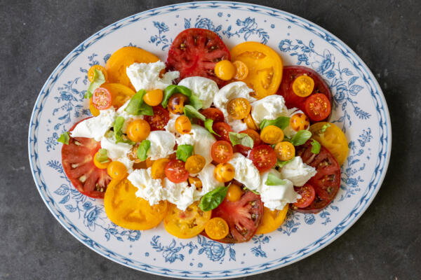 Tomatos, burrata and herbs on a plate.