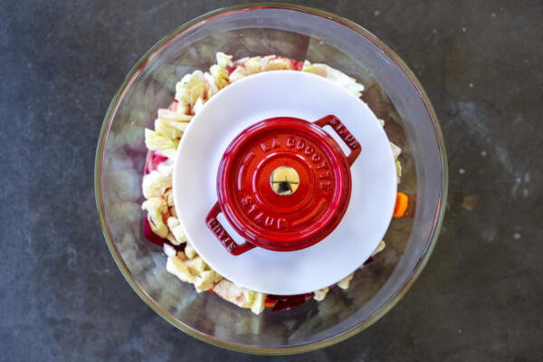 Veggies with marinade in a bowl with weight on top.